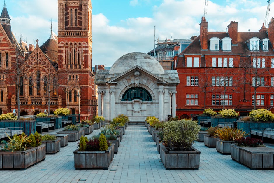 A wide view of an urban flower terrace featuring numerous rectangular wooden planters filled with a variety of blooming flowers and greenery, including yellow, red, and purple hues, arranged along a p
