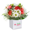 A wave of cheerful energy radiates from this bouquet, as if the spirit of springtime in Aldgate has been gathered and cradled within the embrace of a modern white gift bag. Lush coral and deep red carnations form the heart of the arrangement, their ruffled petals soft and inviting, paired with white daisies whose golden-green centres shine like little beacons of happiness. Drifting amongst these, gentle sprigs of baby's breath add softness and innocence, while closed, purple-tinted blooms on the left hint at flowers just about to open-suggesting both mystery and fresh beginnings. Broad, glossy green leaves fan out to support the entire ensemble, referencing the subtle greenery found along Aldgate's busy streets. The bouquet stands upright, presented in a white gift bag with strong ribbon handles, ready to be delivered for a birthday surprise or sincere thank-you to a friend or colleague in Aldgate. Set against a clean white background, the colours and textures are showcased in their truest form, radiating the joy and optimism of a freshly arranged gift-crafted with a florist's touch that understands the pulse and traditions of this distinctive London neighbourhood.